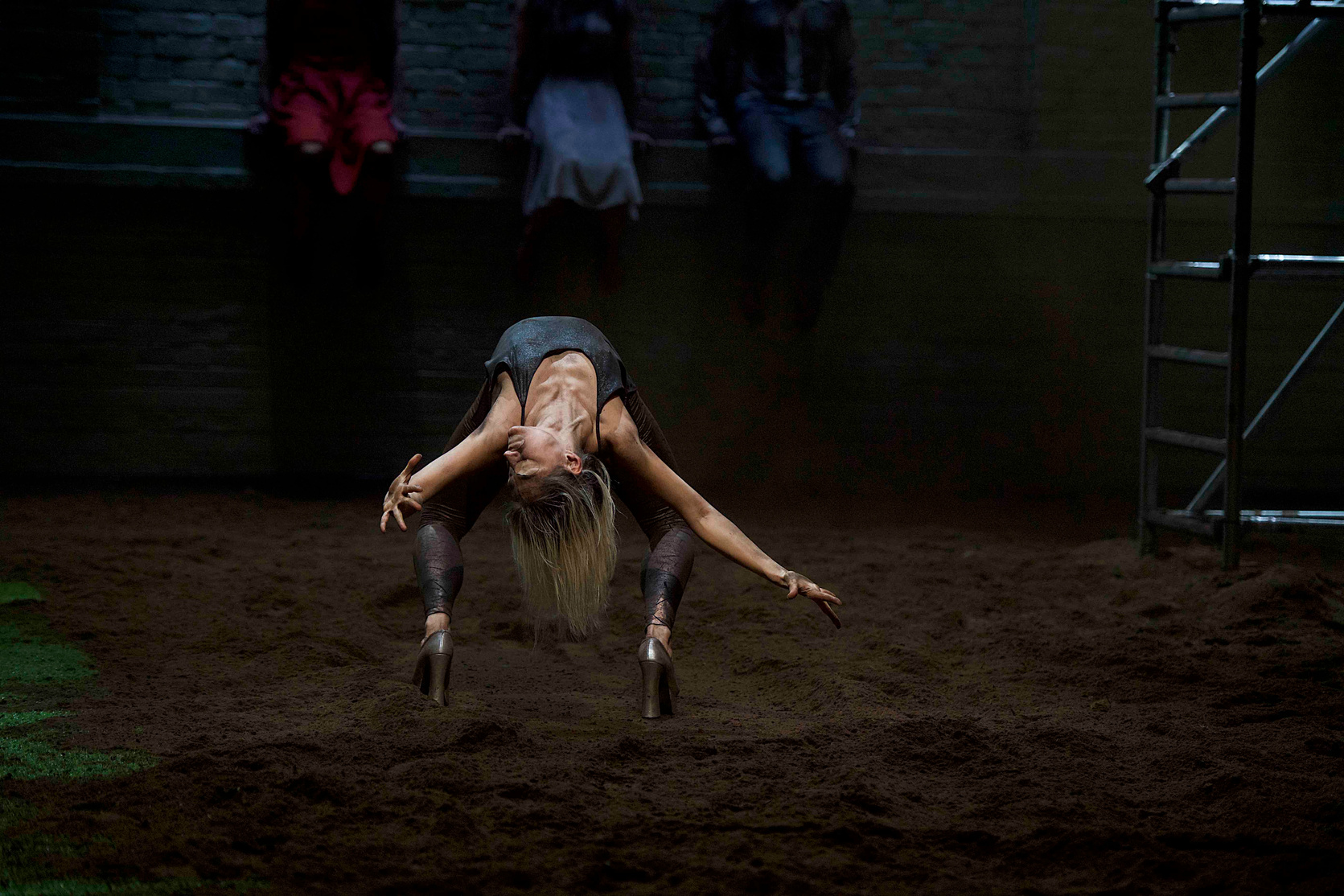 a dancer with eyes covered with tape is doing a backband on a dirt floor