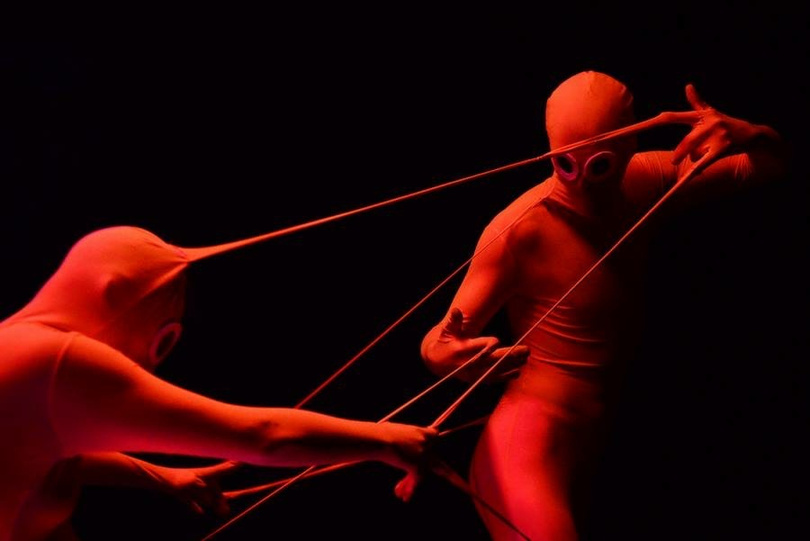 two people in red bodysuits are performing a dance. there are strings coming out of their fingers and their costumes that look like chewing gum