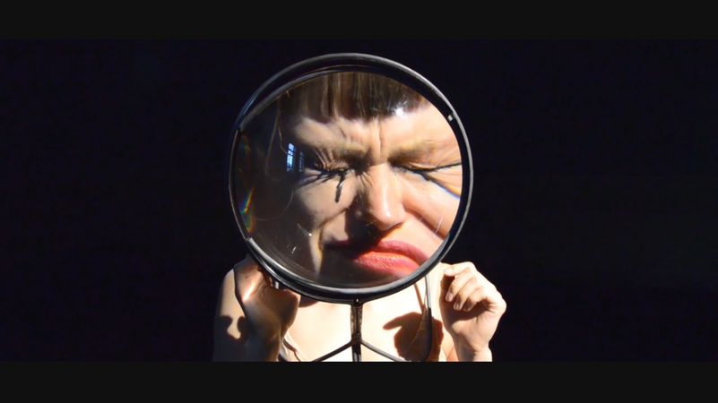 a picture of a person looking into a magnifing mirror with closed eyes