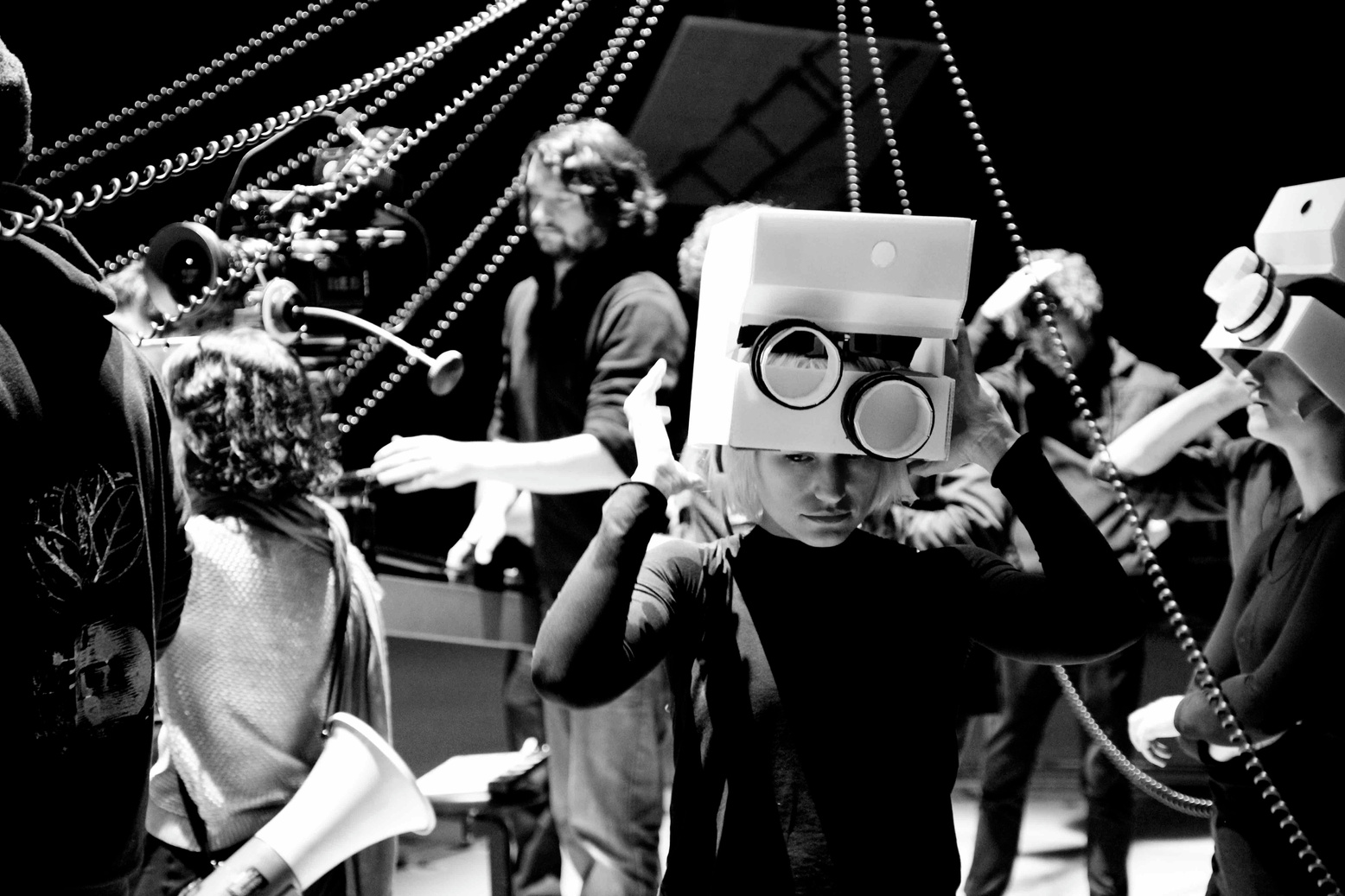 a black and white photo of a group of people and one person in the foreground wearing a cube like helmet