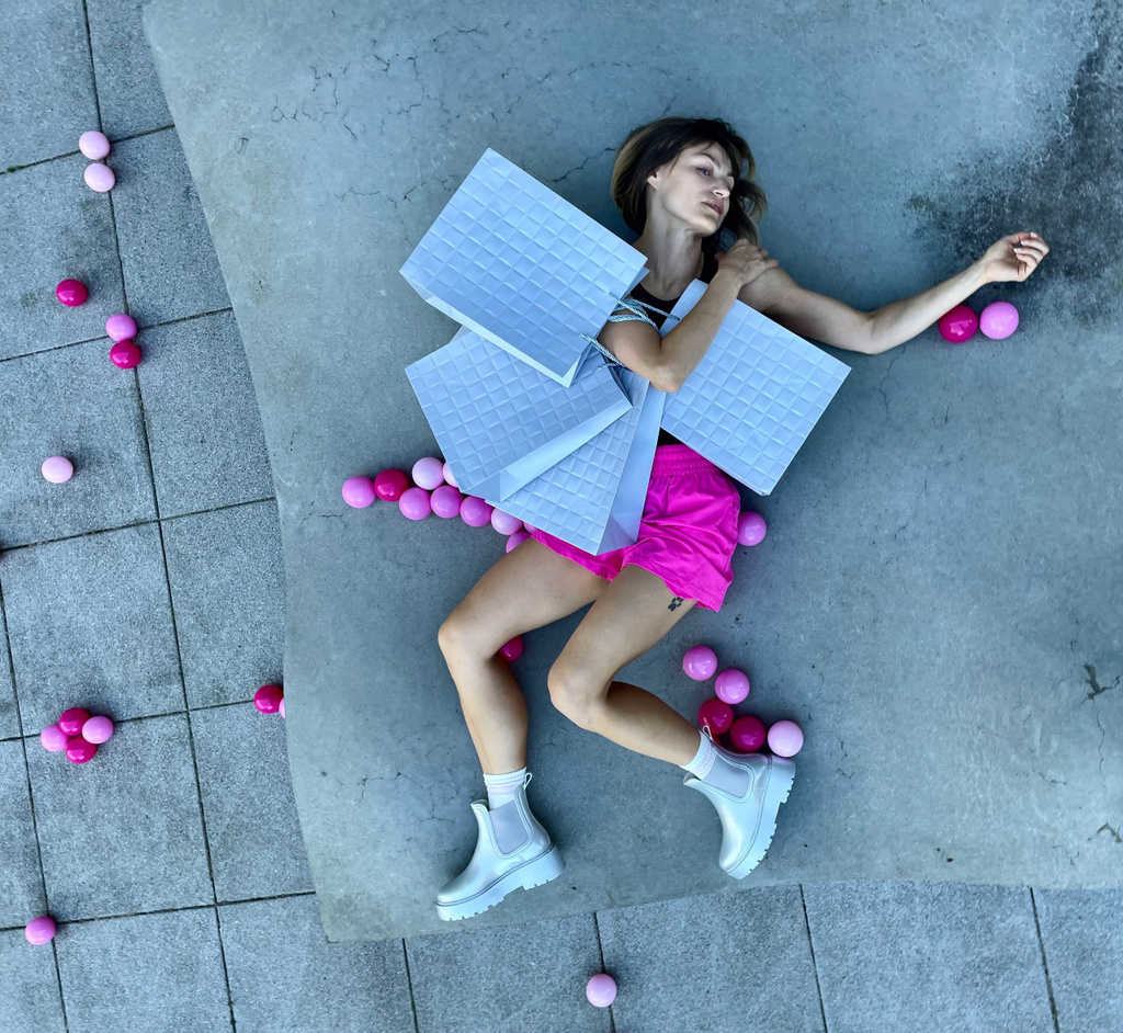 a person - dancer (Karolina Wyrwal), laying on the ground surrounded by pink balls holding gray shopping bags