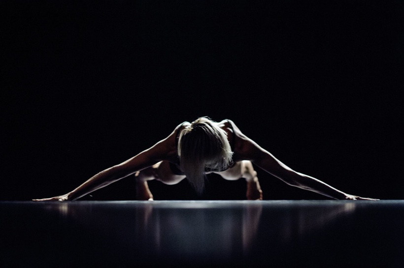 a person: Karolina Wyrwal in a push up position on a dark stage
